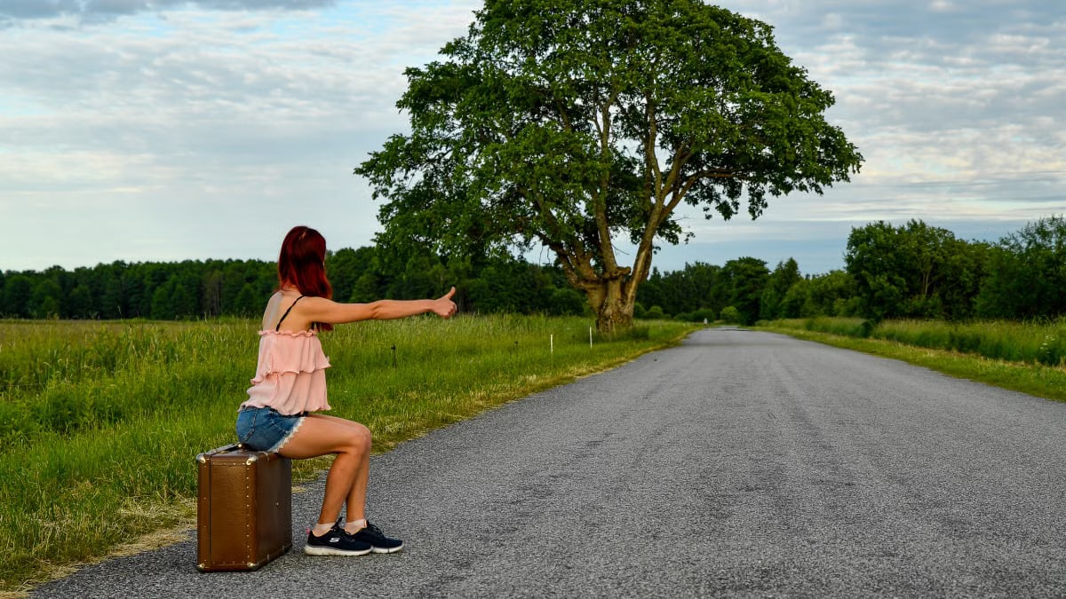A woman hitchhikes on a rural road in Kolga, Estonia, seeking travel adventures.